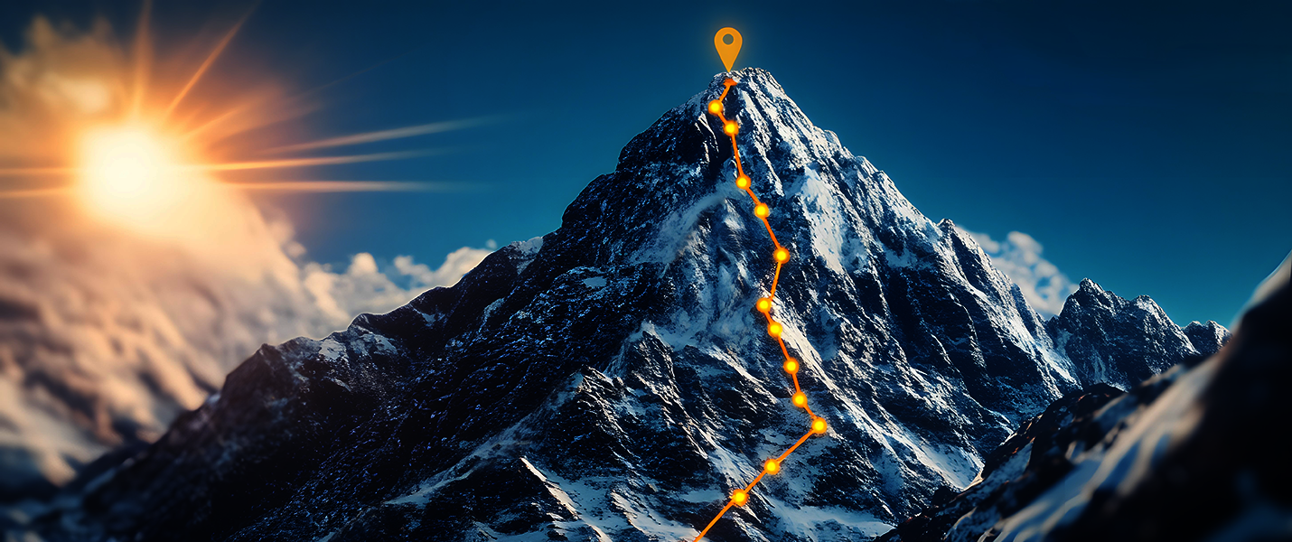 Schneebedeckter Berggipfel mit einer leuchtend orange markierten Route, die vom Fuß zum Gipfel führt; am Gipfel befindet sich eine Markierung. Links ist die Sonne zu sehen, im Hintergrund blauer Himmel und weitere Bergketten.