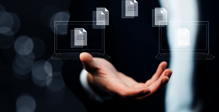 Une main ouverte en costume, sous des documents numériques flottants au-dessus d’ordinateurs portables esquissés, symbolisant le partage et le transfert de fichiers numériques.