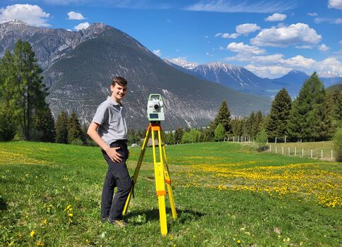Vermesser mit Messgerät steht vor Bergkulisse