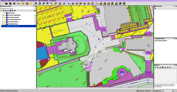 Farbig codierter Lage-/Architekturplan eines Gebäudekomplexes: grüne Freiflächen, gelbe Bauzonen, violette Bauteile, graue Wege und Plätze; zentrale kreuzförmige Gebäudestruktur mit runden Elementen im Umfeld.