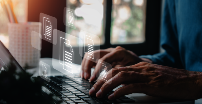 Une personne tape sur un ordinateur portable; autour du clavier flottent des icônes de documents, suggérant la gestion et le partage de fichiers numériques dans un environnement de travail.