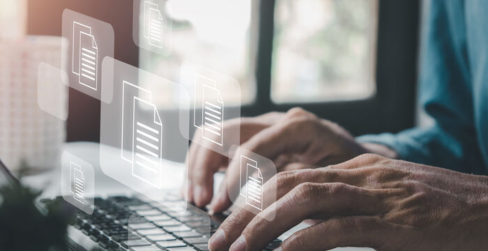 Une personne tape sur un ordinateur portable pendant que des icônes de documents semblent flotter autour de l’écran, suggérant la gestion ou le partage de fichiers numériques.