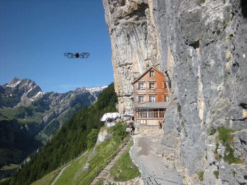 Drohne fliegt im Gebirge und kreist über Berghütte im Fels