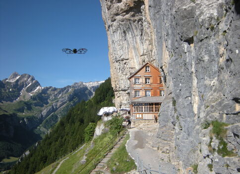 Drohne fliegt im Gebirge und kreist über Berghütte im Fels