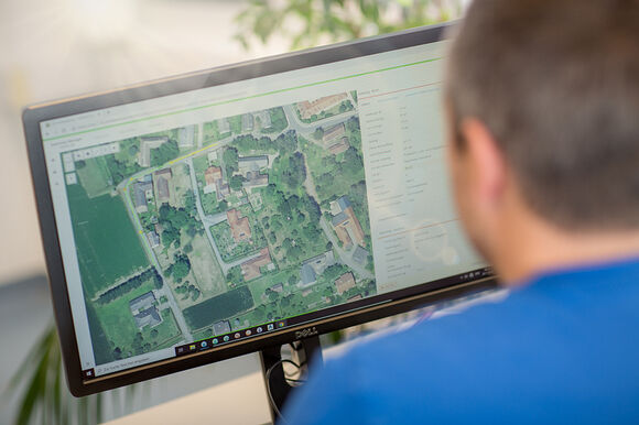 Personne vue de dos regardant un écran d’ordinateur affichant une carte satellite d’un quartier résidentiel avec maisons et espaces verts.