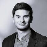 Portrait en noir et blanc d'un homme jeune, cheveux courts, souriant légèrement, vêtu d'une veste sombre et d'une chemise à boutons, posé devant un fond neutre.